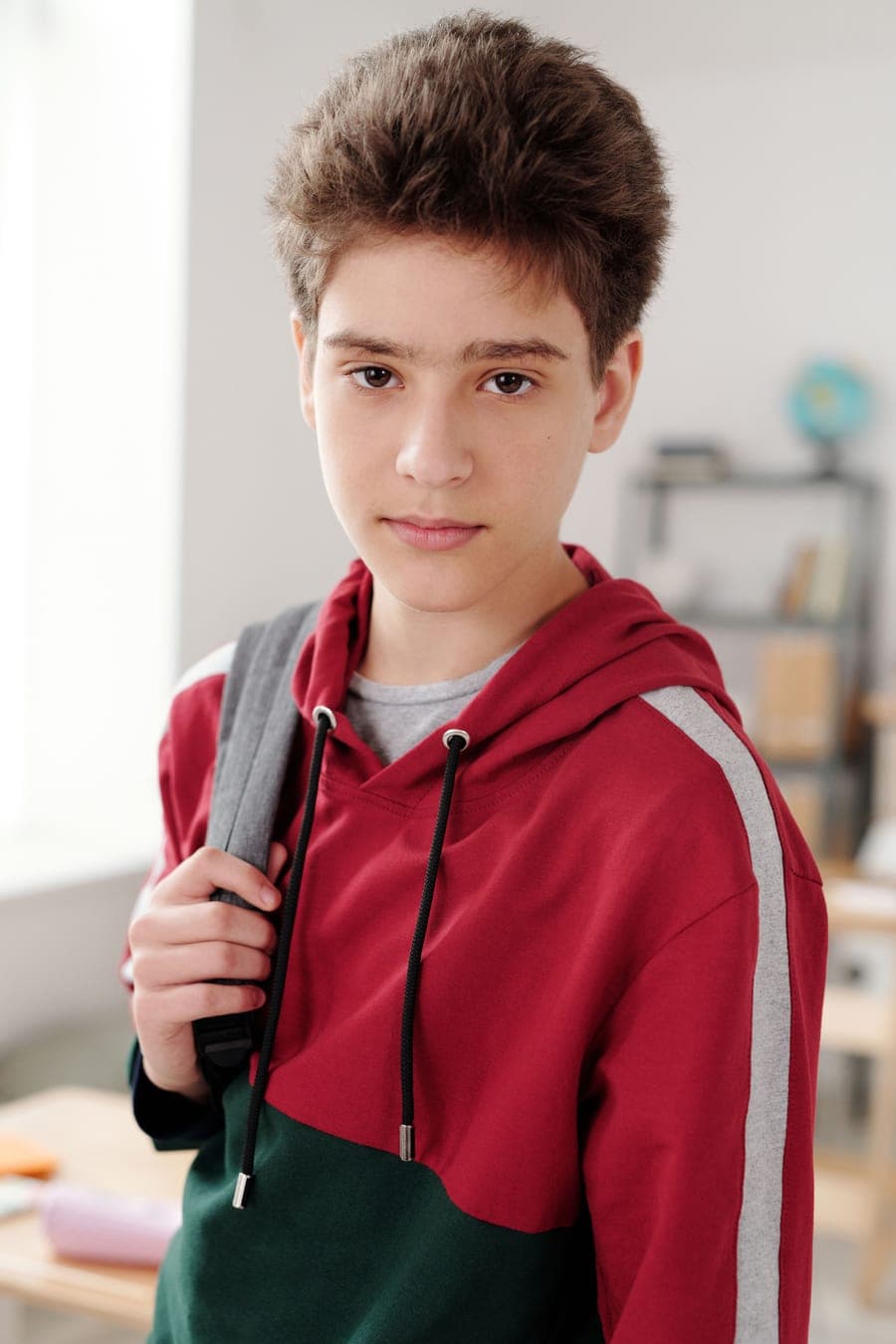A teenage boy in a red and grey hoodie with a backpack over one shoulder