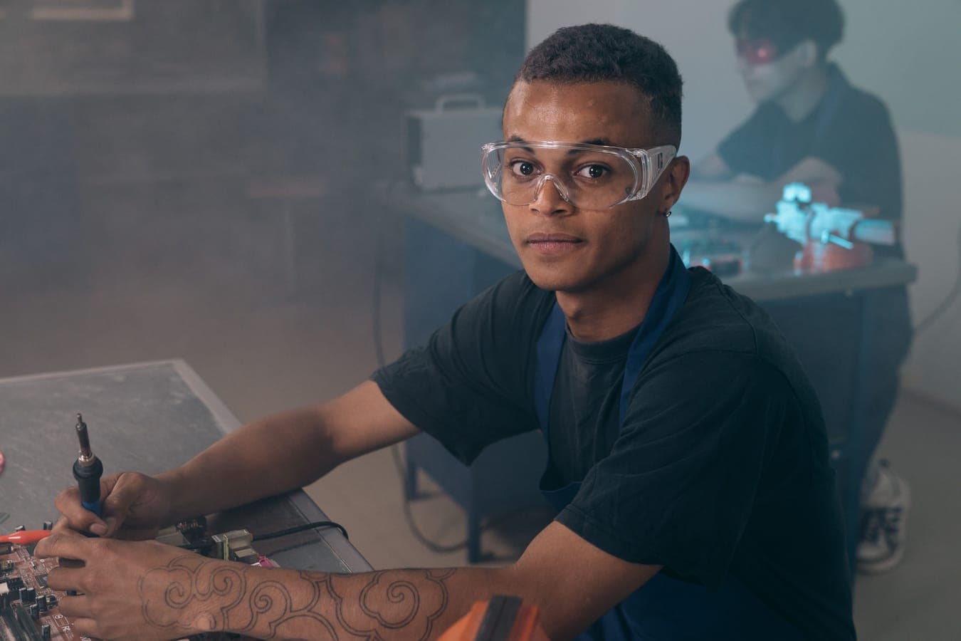 A young man in safety glasses working with a soldering iron at a bench