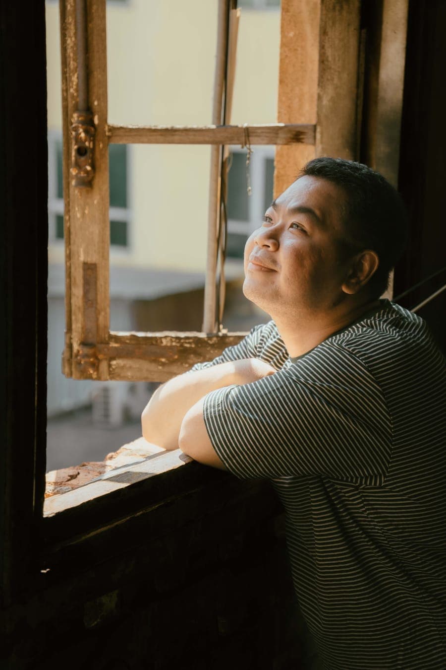 A man smiling as he looks out through an open wooden window