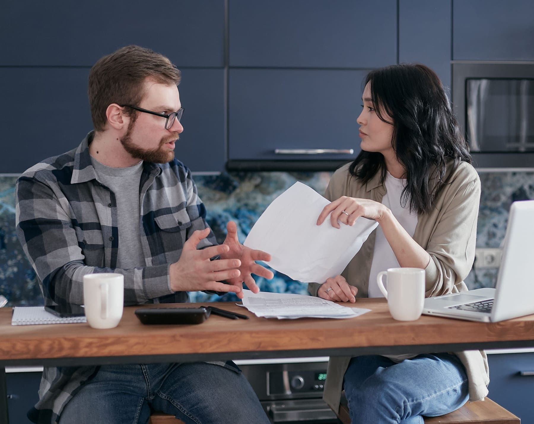 Two adults talking across a kitchen table, working through paperwork together over coffee
