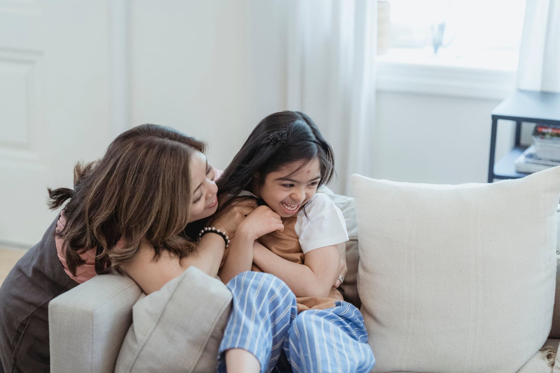 A mother and her teenage daughter laughing together as they sit close on a sofa